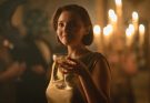 "Woman in a gold dress holding a drink at an elegant, dimly lit party with candlelight in the background, creating a warm, sophisticated atmosphere."