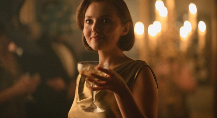 "Woman in a gold dress holding a drink at an elegant, dimly lit party with candlelight in the background, creating a warm, sophisticated atmosphere."